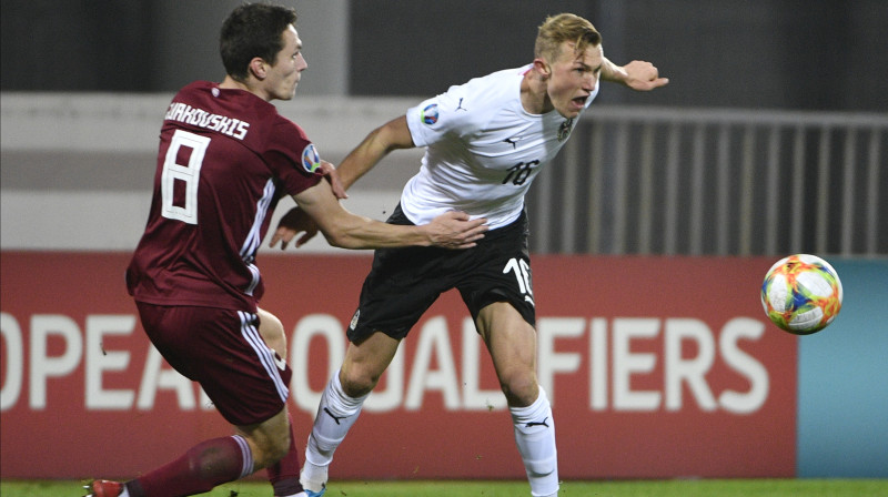 Raivis Andris Jurkovskis (Nr. 8) cīņā ar Austrijas izlases futbolistu. Foto: Romāns Kokšarovs/F64